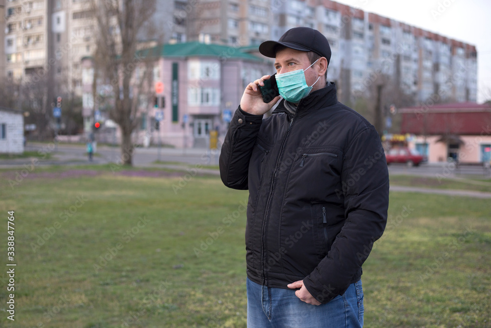 Portrait of man in medical mask stands alone in park and speaks on the phone. Coronavirus epidemic Portrait of man in medical mask stands alone in park and speaks on the phone. Coronavirus epidemic