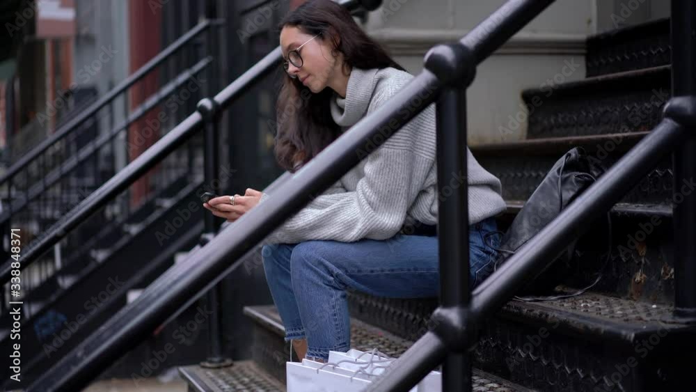 Charming hipster girl in optical spectacles sitting at stairs in metropolitan downtown and typing text message during free time for blogging via cellular device, Caucasian woman searching information Charming hipster girl in optical spectacles sitting at stairs in metropolitan downtown and typing text message during free time for blogging via cellular device, Caucasian woman searching information