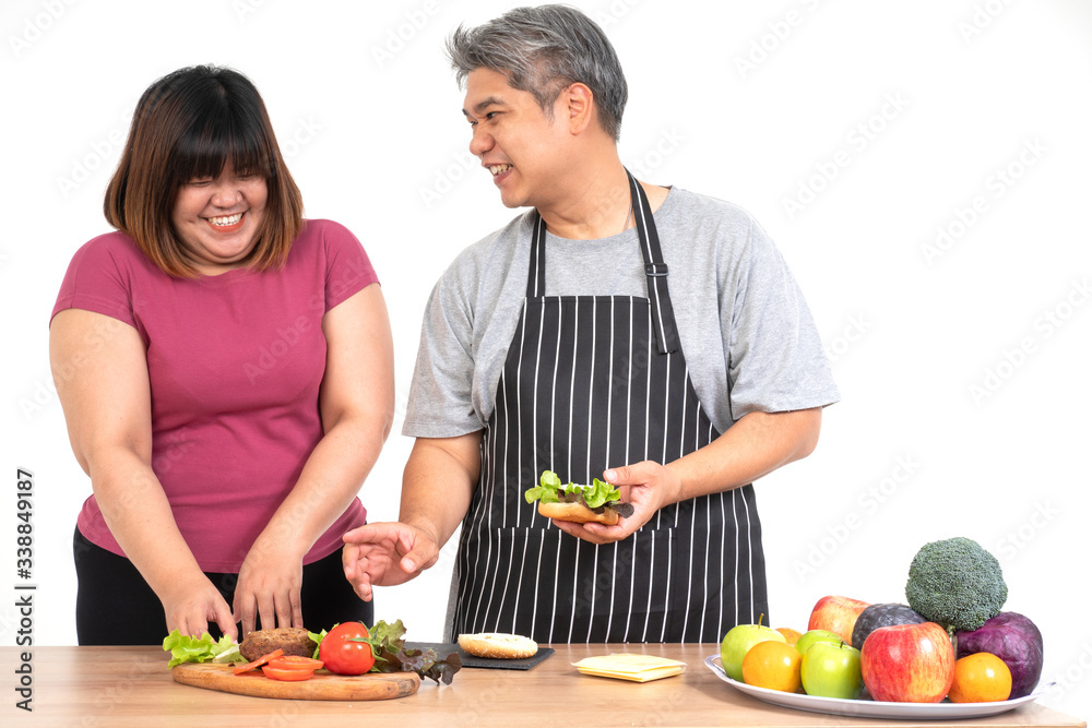 Happy overweight couple cooking a burger in the kitchen room. A vegetable on the table. Concept of happy family and binge eating Happy overweight couple cooking a burger in the kitchen room. A vegetable on the table. Concept of happy family and binge eating