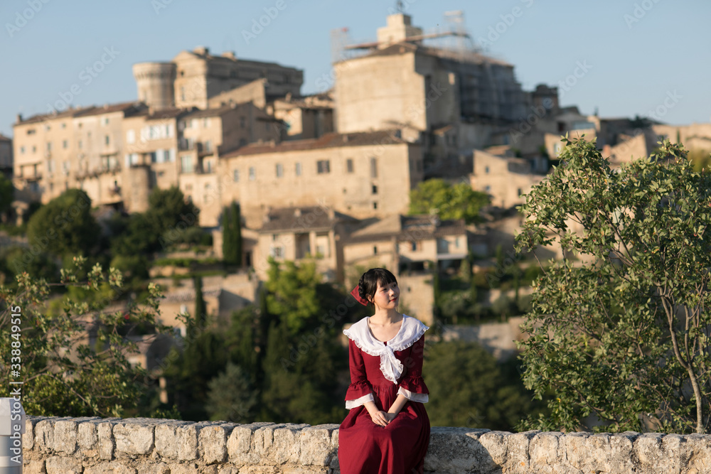 Young Asian woman in red dress, sitting at the edge of cliff outside the ancient village of Gordes, Provence, France