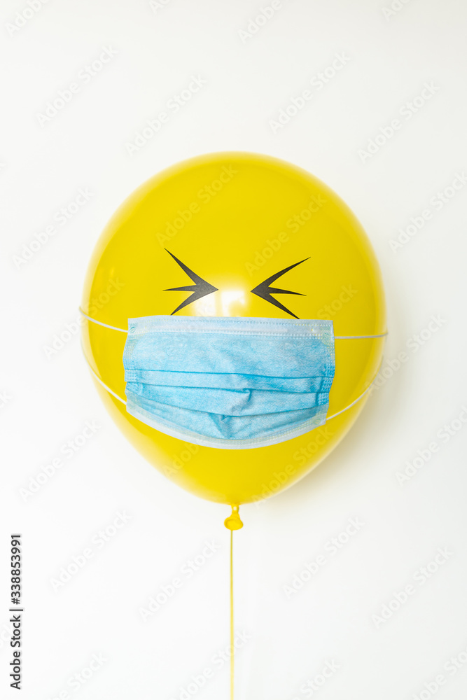 Yellow balloon with medical mask and doodle eyes. Conceptual image of Birthday party during Corona virus quarantine lockdown Yellow balloon with medical mask and doodle eyes. Conceptual image of Birthday party during Corona virus quarantine lockdown