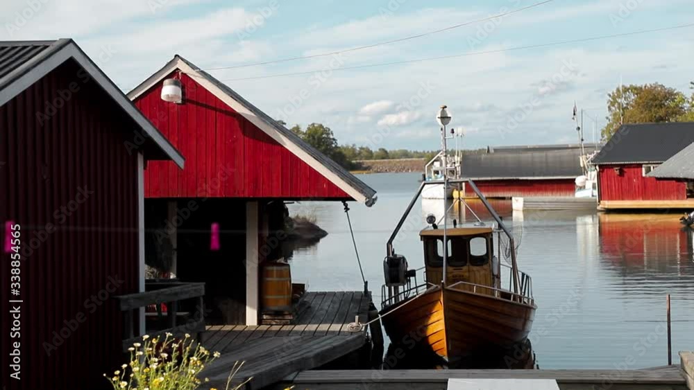 Small yellow fishing boat lays peacefully in a small harbour surrounded by typical Swedish Falu red houses. Camera pan through traditional harbor in Sweden with a single boat Small yellow fishing boat lays peacefully in a small harbour surrounded by typical Swedish Falu red houses. Camera pan through traditional harbor in Sweden with a single boat