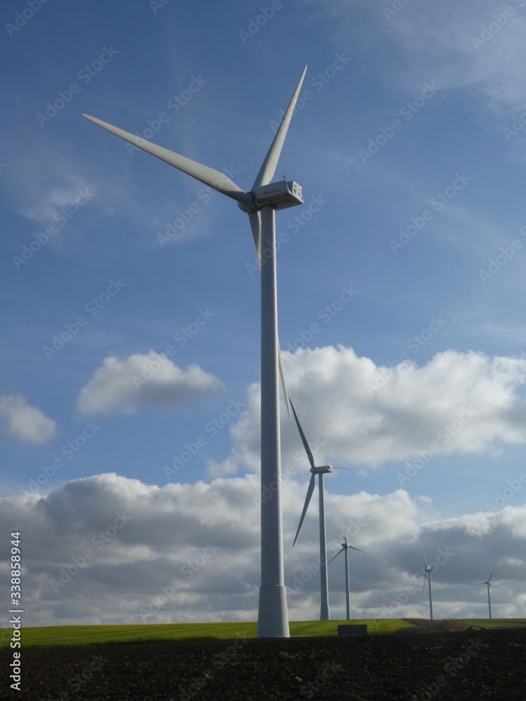 Row of five wind turbines in a blue sky with cottony clouds Row of five wind turbines in a blue sky with cottony clouds