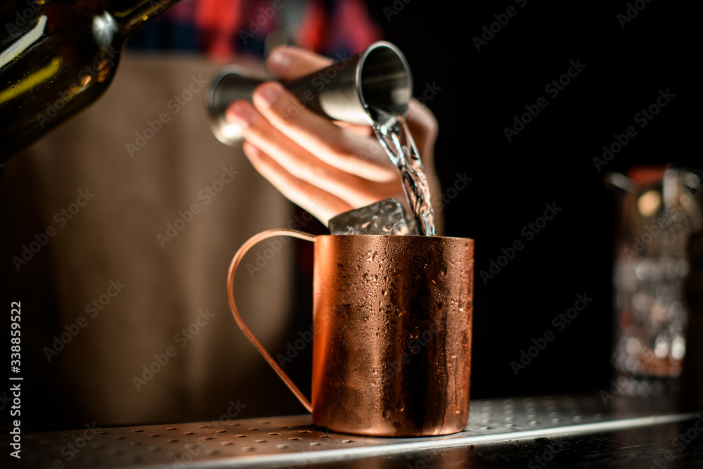 close-up metal cup into which bartender pouring liquid