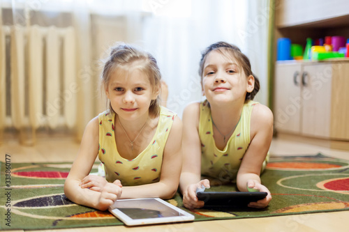Two sisters playing in gadgets on carpet in living room