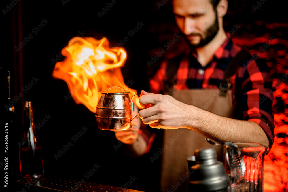 bartender holds metal cup with cocktail and sets it on fire.