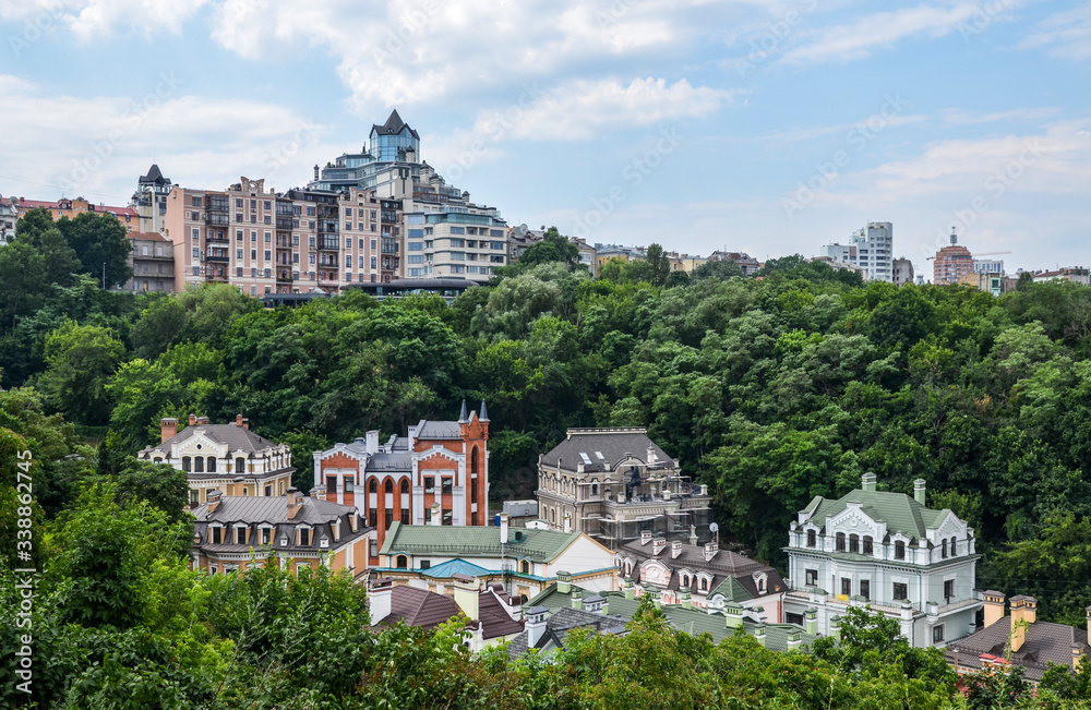 Cute and colorful beautiful houses surrounded by trees at Vozdvizhenka and modern residential buildings on background. Summer Time in historical part of Kyiv - Podol 