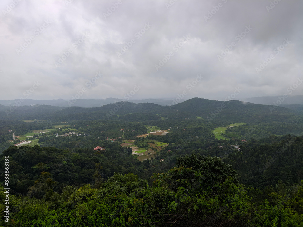 A landscape view of green hills with cloudy sky on the background in Coorg, India.
