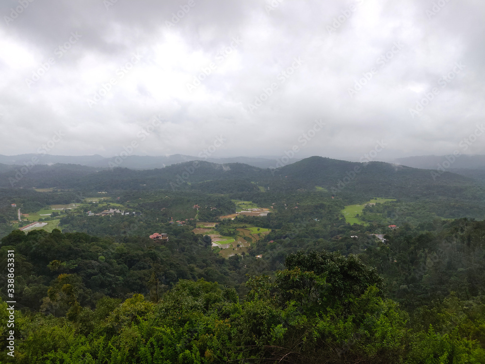 A landscape view of green hills with cloudy sky on the background in Coorg, India.