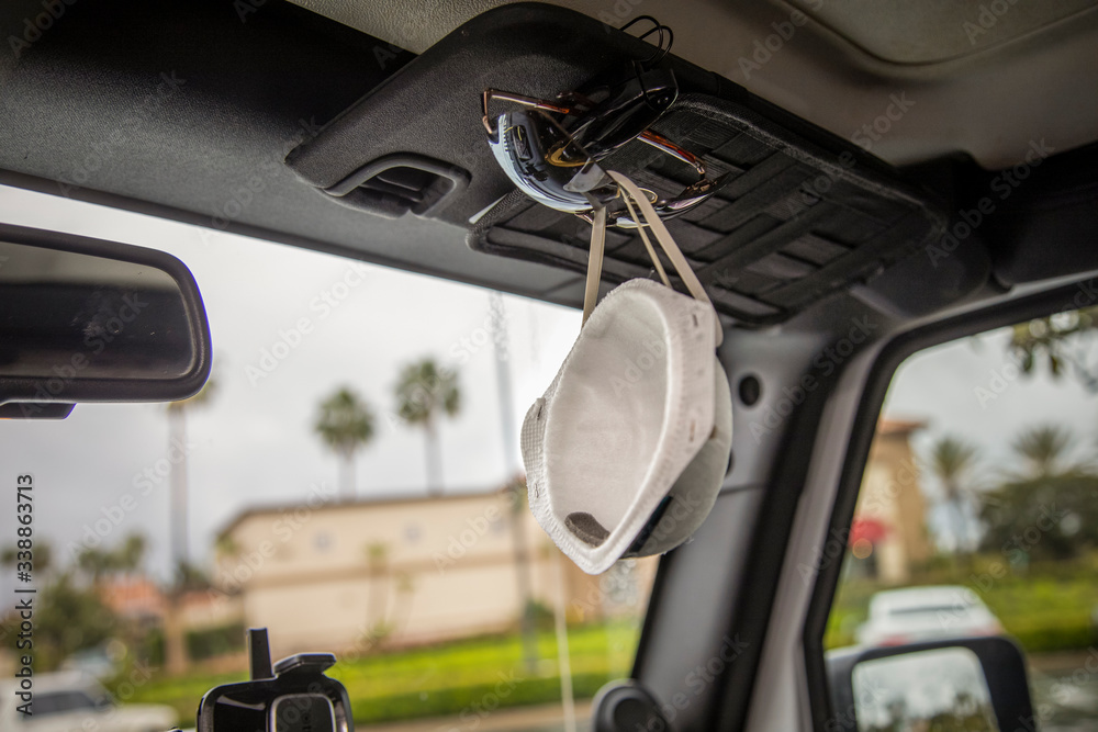 Face mask clipped with sunglasses on visor of interior of a car in a shooping center parking lot during the Coronavirus pandemic Face mask clipped with sunglasses on visor of interior of a car in a shooping center parking lot during the Coronavirus pandemic