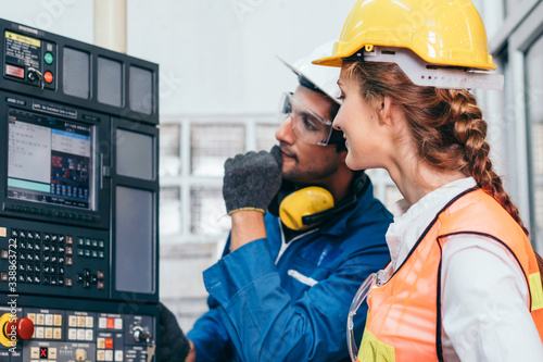 Male industrial engineer or technician worker in hard helmet training female trainee assistant using control machine. Man and woman technician people working in heavy industry manufacturing factory. photo