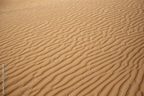 The surface of the orange sandy dunes with parallel lines made by wind.