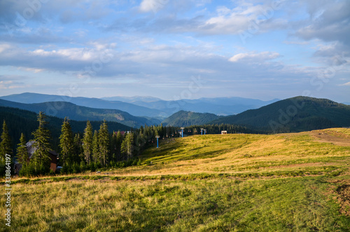 View to the ski lift on the background of a beautiful summer day on the famous ski resort. Green fir trees and houses of the village Dragobrat Carpathian mountains, Ukraine 