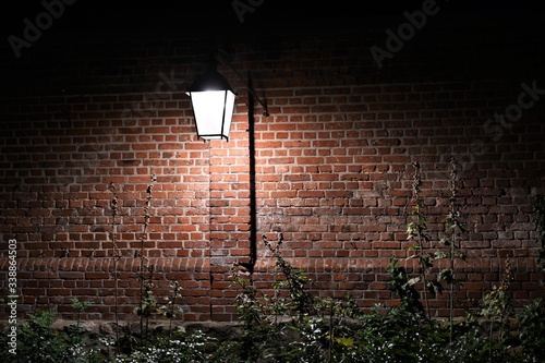 Leuchtende Lampe (Laterne) vor einer rot gemauerten Wand bei Nacht