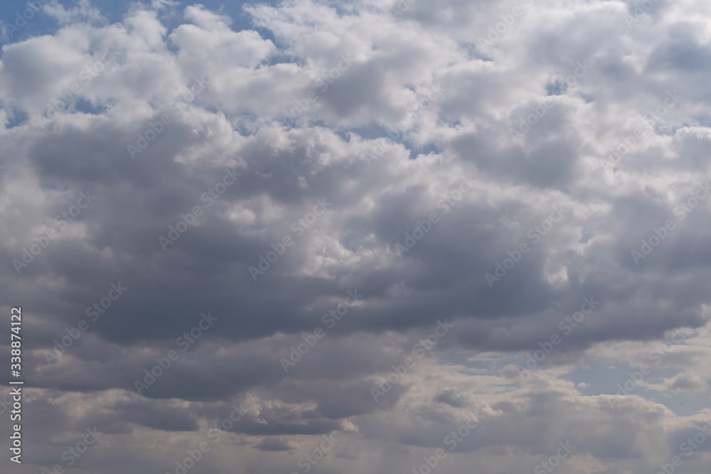Many Cumulus and rain clouds of various shapes, sizes, and colors covered the blue sky. On the right side, the sun's rays break through from above. In the distance, the rain begins to fall.