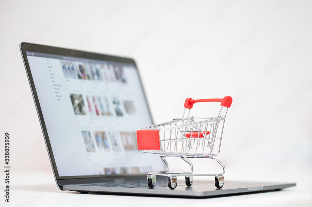 Red trolley on laptop keyboard.A cart and notebook computer on white background.Electronic commerce that allows consumers to directly buy goods from a seller over the internet.Shopping online concept.