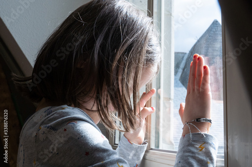Fotografia Little girl looking through the window with anxiety during coronavirus quarantine in the house