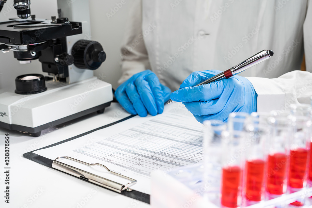 Top view at the doctor's workplace. Test tubes with blood tests, the doctor writes the results in the form Top view at the doctor's workplace. Test tubes with blood tests, the doctor writes the results in the form