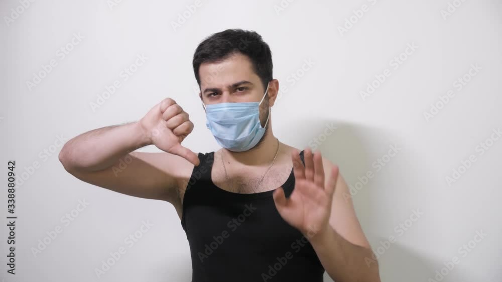 Caucasian man puts on his medical mask looks into camera and one thumb down Covid19 Coronavirus Caucasian man puts on his medical mask looks into camera and one thumb down Covid19 Coronavirus