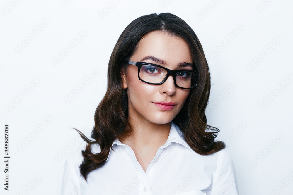 Portrait of young brunette woman with a healthy clean skin. Young beautiful business woman in stylish glasses and white shirt posing in studio. Portrait of young brunette woman with a healthy clean skin. Young beautiful business woman in stylish glasses and white shirt posing in studio.
