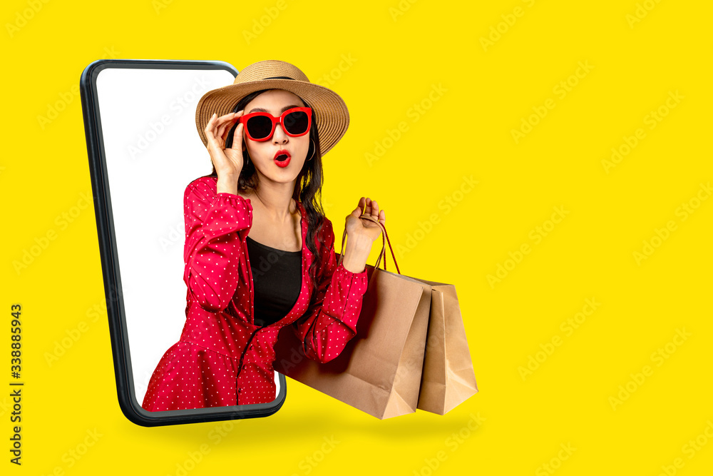 Young attractive asian female holding shopping bag feeling excited, happy  and amaze on beauty or fashion online store discount promotion with concept  tech on omnichannel e-commerce thru mobile screen. Stock Photo