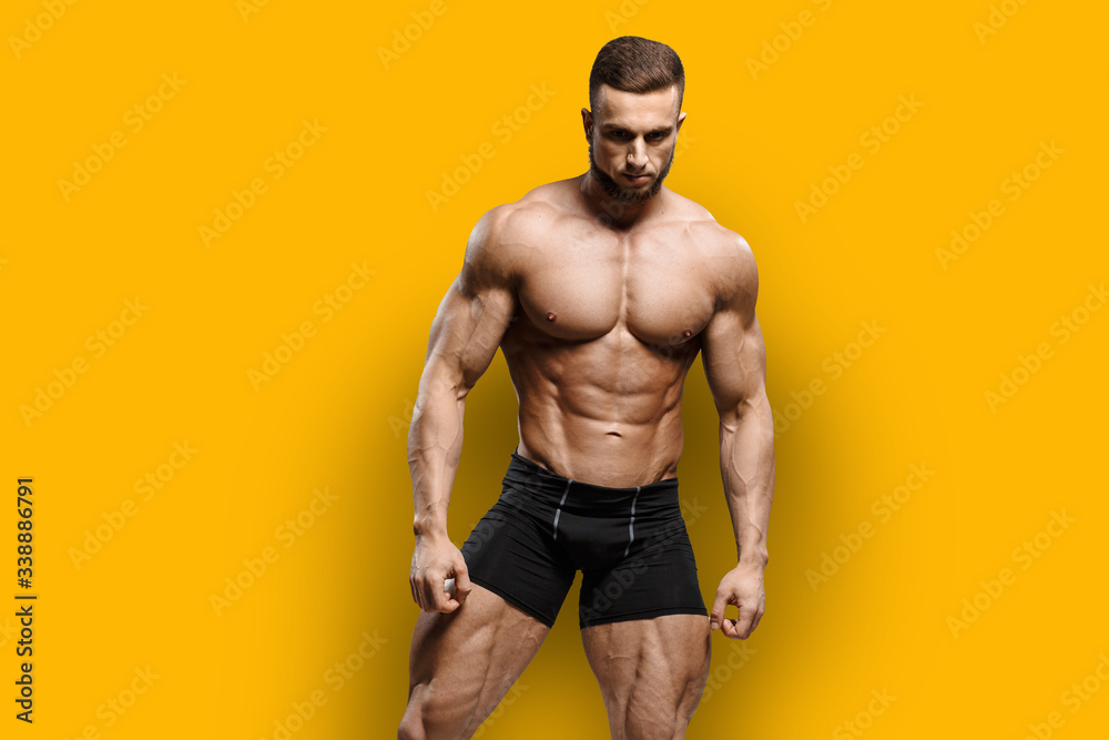 Muscular bodybuilder fitness man with perfect body  shows muscles isolated over yellow background. Workout bodybuilding concept. - obrazy, fototapety, plakaty 