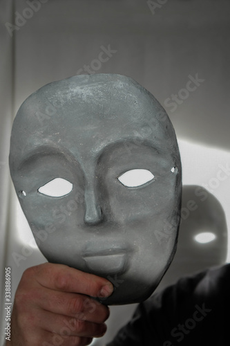 Black clay mask in a man's hand. Mask on a white background in a sunny morning in Ukraine. A clear shadow from the mask.