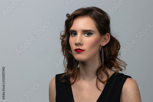Beautiful young girl with long curly hair in a black long dress posing on grey background. Concept of hairstyling in salon and face care