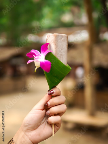 The hand holding Ice cream decorated with banana leaves and flowers.