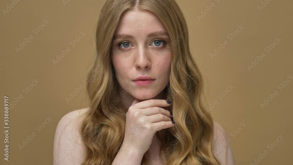 A beautiful young half-naked woman with long hair is posing to the camera isolated over beige background A beautiful young half-naked woman with long hair is posing to the camera isolated over beige background