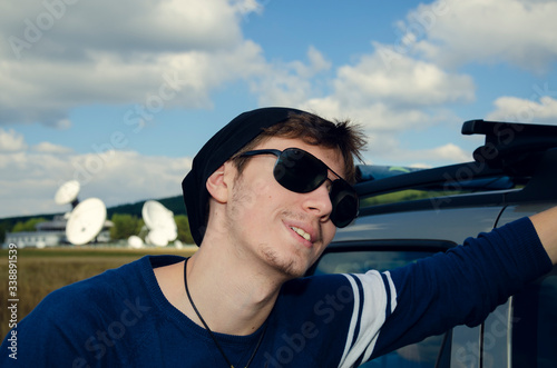 Young Caucasian man with sunglasses leaning on the car roof and smiling Selective focus