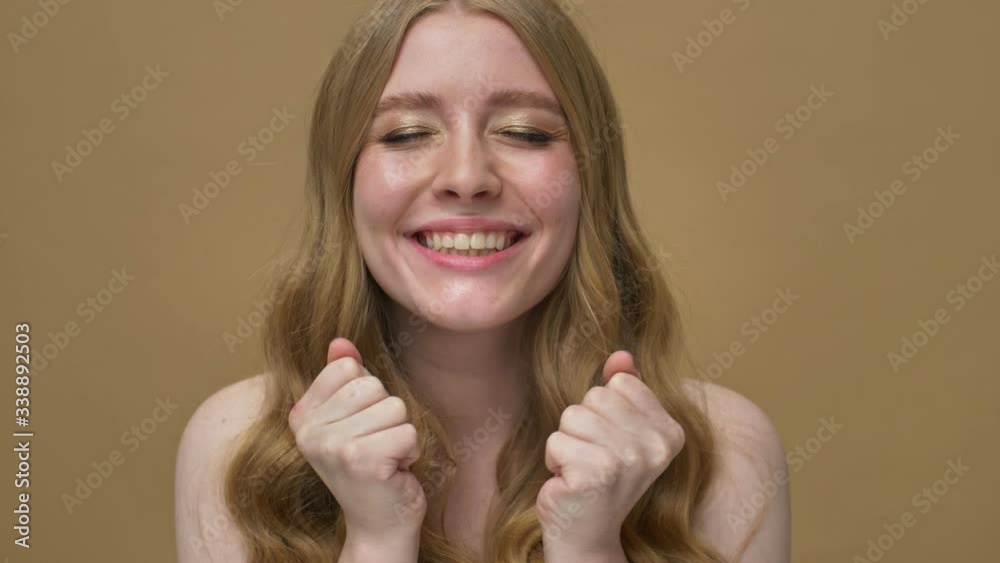 A happy smiling young half-naked woman with long hair is rejoicing while looking to the camera isolated over beige background A happy smiling young half-naked woman with long hair is rejoicing while looking to the camera isolated over beige background