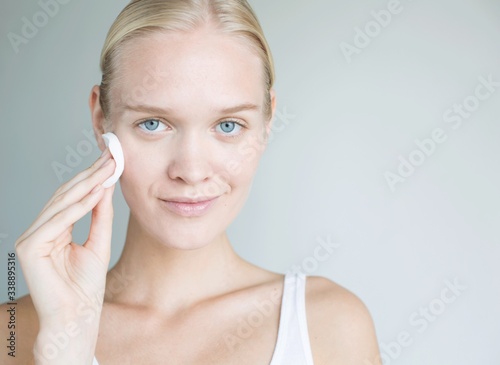 Blonde woman using cotton pad on her face. Beautiful model using cotton pad. Healthy woman using treatment on her face. 