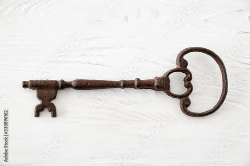 Old rusty key on aged white wooden background. © Fotografos