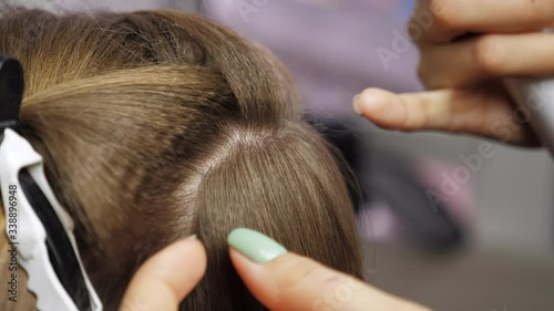 Close up professional hairstylist makes waves curling on a woman's hair. The girl in the beauty salon takes a lock of hair and presses it with a hair straightener. 4K footage photo