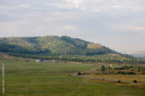 Suburb and villages. Big mountains and green forests. Trees and their shadows on the grass. Summer day with dark blue and grey sky and clouds. Fields. Fresh air.