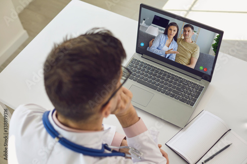 Doctor medical online call.Shoulder view doctor therapist psychologist speaks with couple video chat using a laptop in a clinic office.