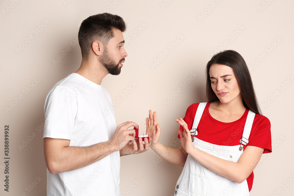 Young woman rejecting engagement ring from boyfriend on beige background Young woman rejecting engagement ring from boyfriend on beige background
