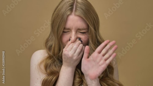 A beautiful young half-naked woman with long hair is feeling a stench and covering her nose with her hand isolated over beige background