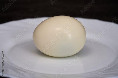 Isolated peeled boiled chicken egg on a white plate, food macro, closeup.