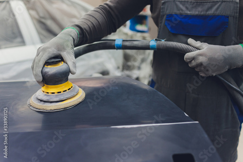 Auto mechanic preparing the car for paint job by applying polish with the power buffer machine