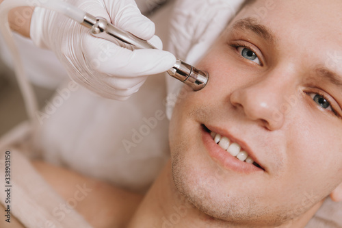Cropped close up of a young cheerful man smiling while cosmetologist performing facial skincare treatment