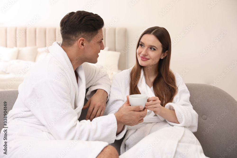 Happy couple in bathrobes with coffee on sofa at home