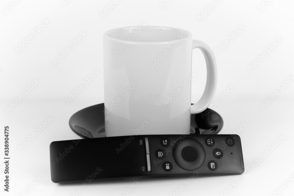 White coffee cup on a black plate and a remote control