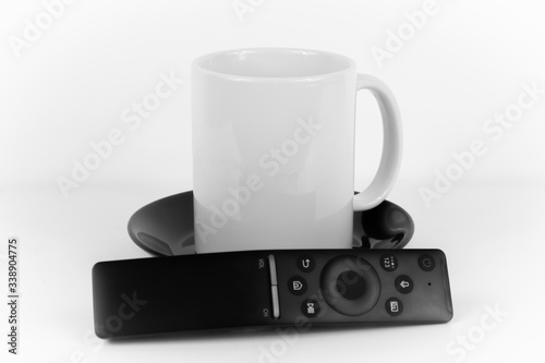 Obraz na płótnie White coffee cup on a black plate and a remote control w salonie