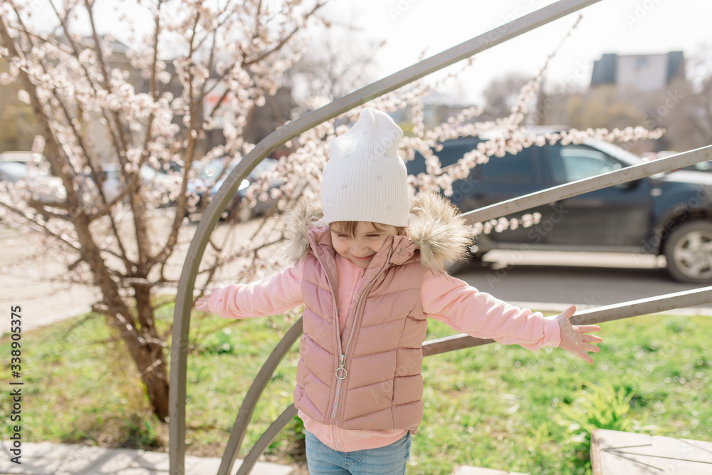 Little girl walks on a background of a blossoming tree in spring
