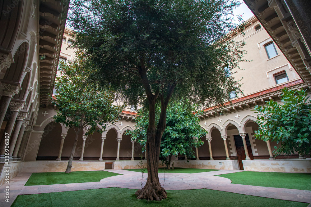 Courtyard in a cloister in Barcelona with trees and an elegant arch.