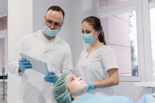 Young woman getting dental treatment in clinic  denist and assistant using digital tablet