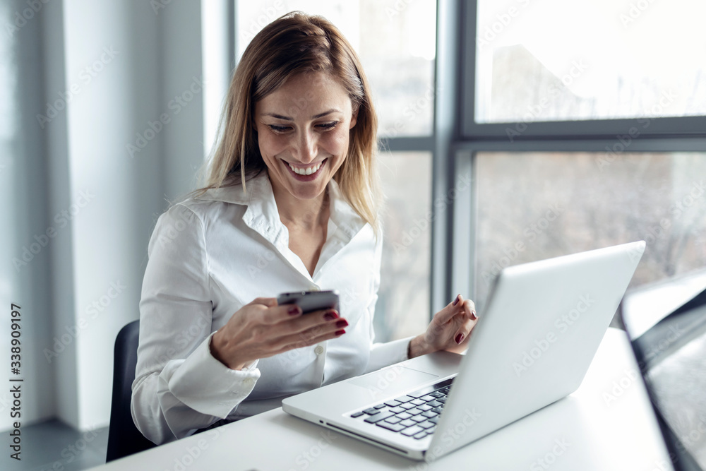 Businesswoman sitting in office working on laptop, using smartphone Businesswoman sitting in office working on laptop, using smartphone