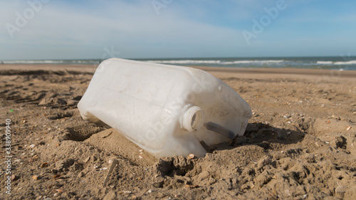 plastic liquid container discarded on a sandy beach with sea and blue sky in background